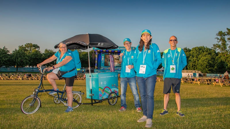 One person on a bike with a mini display trailer and black umbrella. There are 3 other people in the picture and all are wearing light blue Uefa Euro 2020 branding.