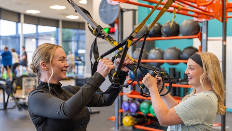 2 people are standing in a gym looking and smiling at each other pulling on ropes