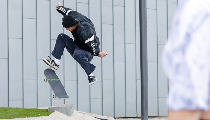 A skateboarder performs a stunt in the background as an onlooker watches on