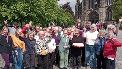A large group of volunteers standing outside Glasgow Cathedral, smiling and waving at the camera