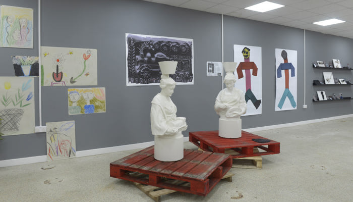 Two statues of "mother Glasgows" are displayed on red pallets. In the background there are painting and prints. 