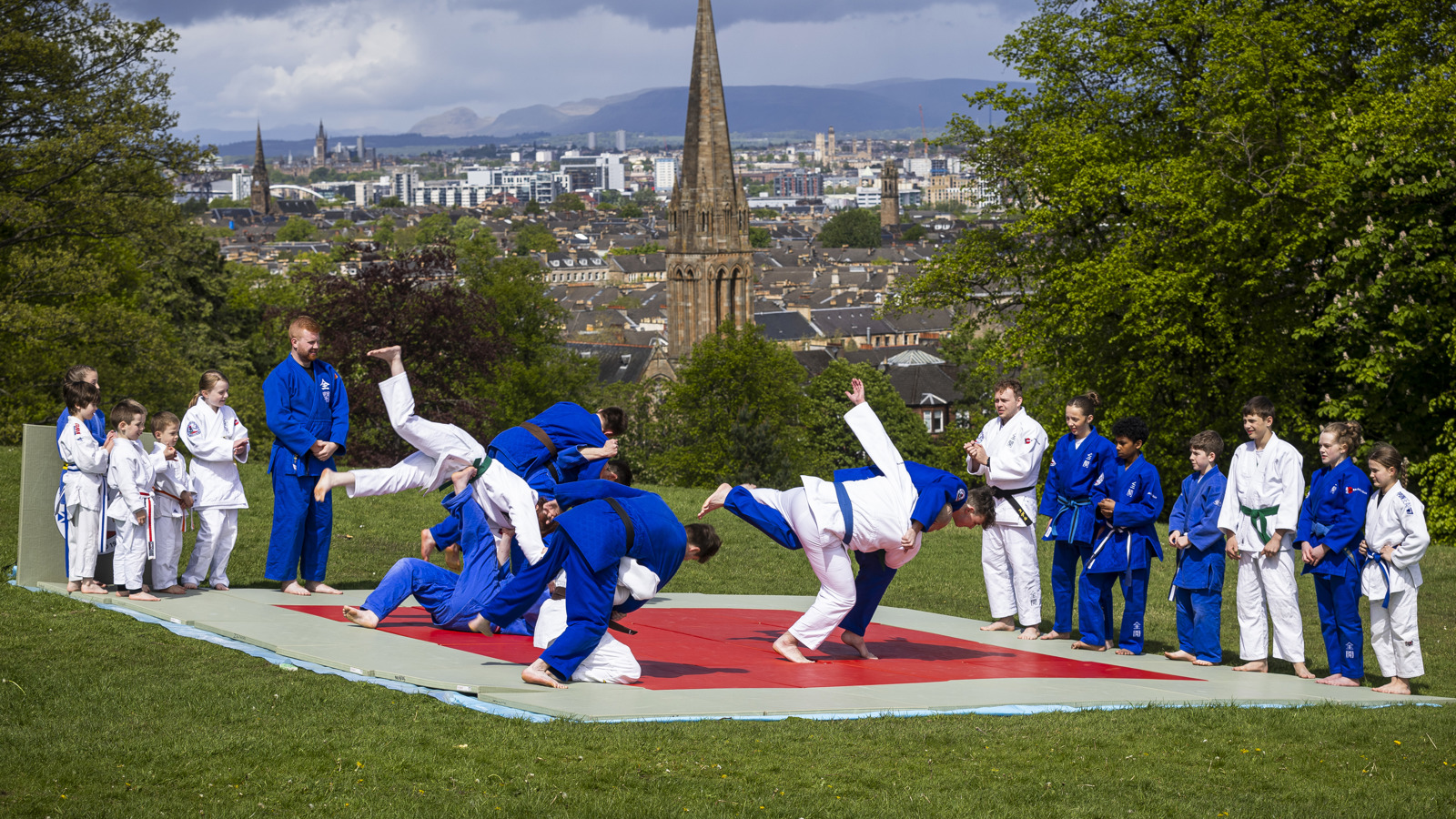 People are taking part in a judo session on a hilltop overlooking a cityscape