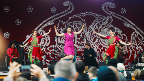 Dancers in multicoloured costumes perform in front of a large crowd
