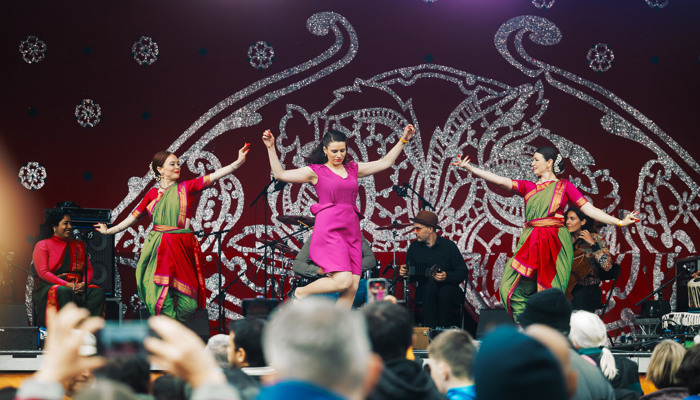 Dancers in multicoloured costumes perform in front of a large crowd