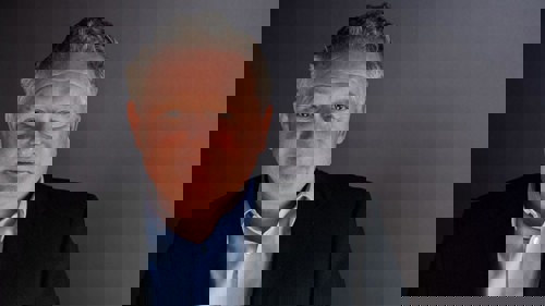 Headshot of a person wearing a light shirt and a dark suit jacket