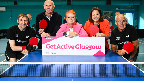 Men and women stand at the end of a table tennis table with a sign which reads 'Get Active Glasgow'