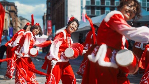 Dancers in red and white outfits form a line during a community arts, comedy, circus, dance and live music festival