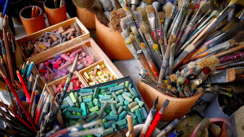 A close-up of multi-coloured chalk, paint brushes and pencils. 