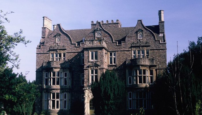 a photograph of a medium sized country house. It has 3 storeys, a protruding room on the front elevation and single bay windows on either side