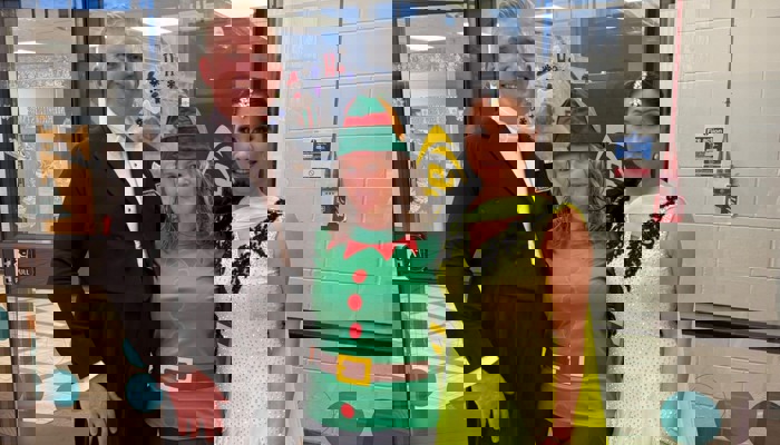 A pair of professional ballroom dancers in costume posing for a photo with a person dressed as a Christmas elf