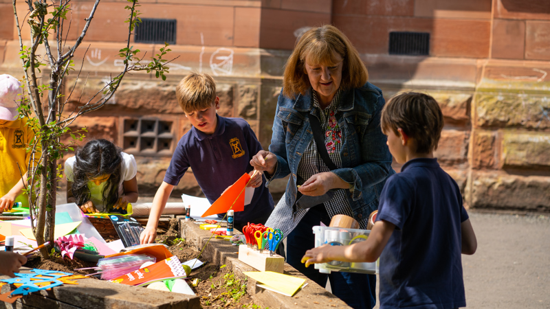 An adult helps young children at a primary school plant seeds in a raised bed. 