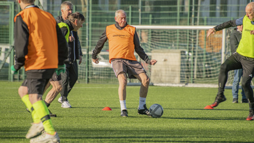 People wearing brightly coloured bibs during a game of Walking Football outside on an artificial grass pitch.