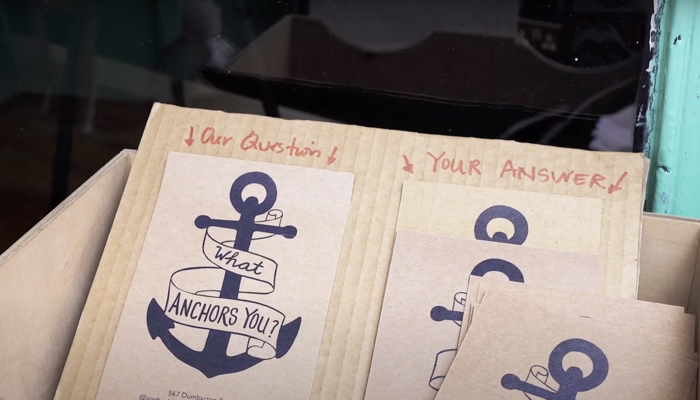 Specially made postcards sit in a box. They show an anchor with a banner wrapped around it reading "what anchors you?"