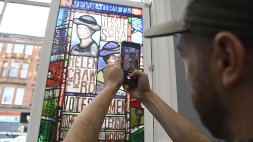 Person in a baseball cap using a smartphone to take a picture of a colourful stained glass window