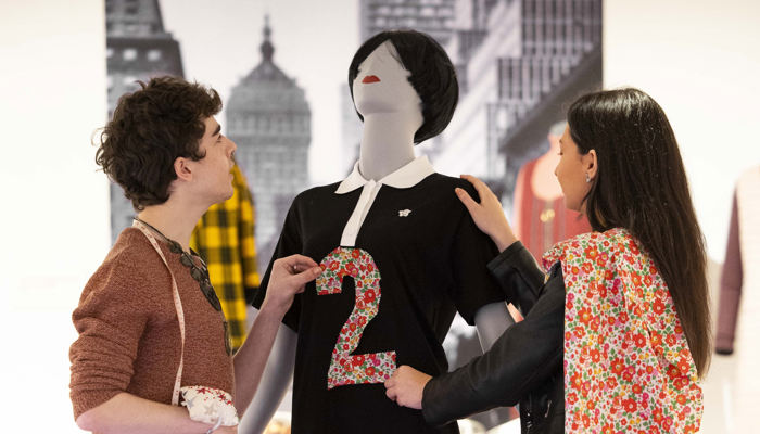 Two students adjusting a dress on a tailors model. The dress is black with a white collar in the style of Mary Quant.