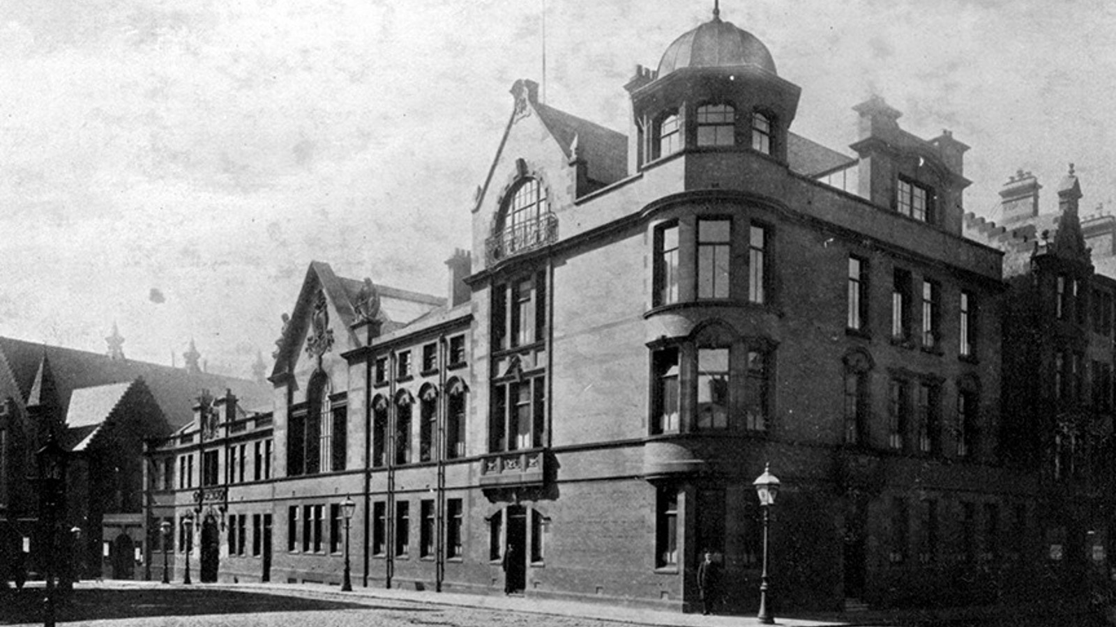A sandstone building on the corner of a cobbled street with a police officer standing at the entrance.