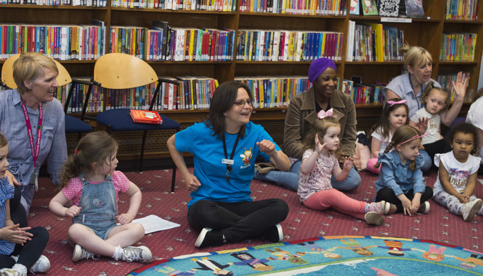 a group of adults and children sitting on the floor in a library taking part in an interactive class