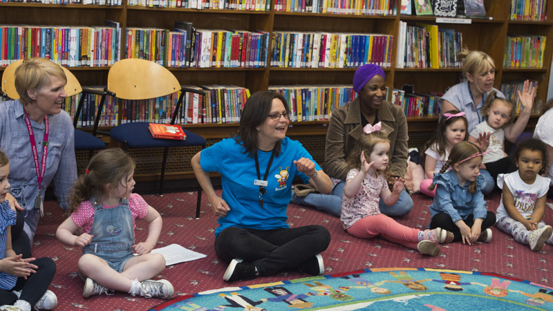 a group of adults and children sitting on the floor in a library taking part in an interactive class