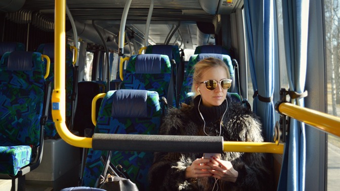 A young person in sunglasses is sitting on a bus.