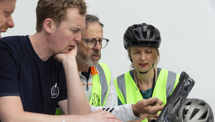 Three people look at an ipad with cycling helmets on. 