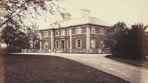 A black and white photo of Cathkin House which has white railings around it, a path leading up to the entrance plus a large lawn with mature trees and shrubs.