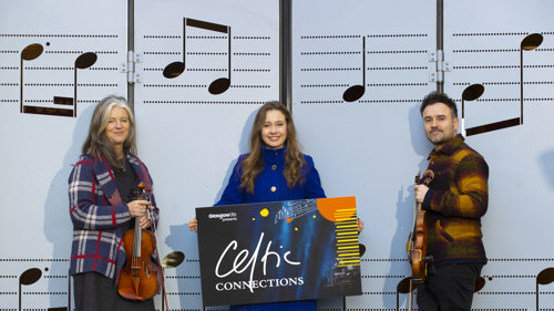 Three musicians standing in front of large-format sheet music showing notes