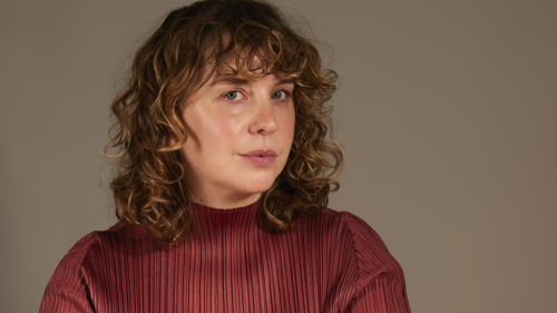 A woman with shoulder-length hair is wearing a red top and looking at the camera