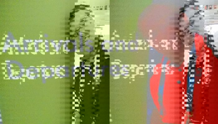 Andrew McVie wearing his red Clyde-sider uniform in front of the arrivals and departures sign at Glasgow Airport during the 2014 Commonwealth Games.