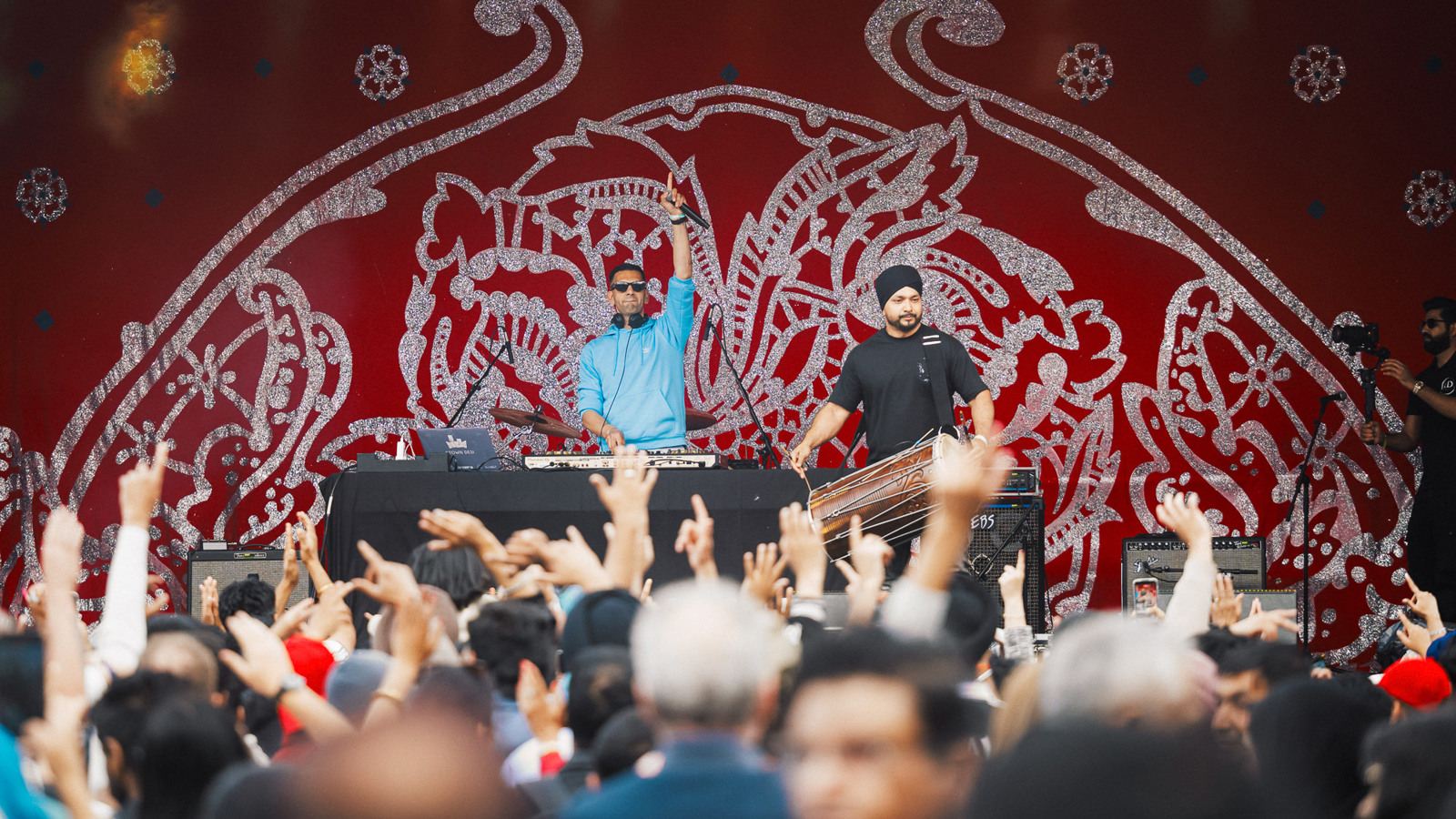A DJ plays in front of music fans who are raising their hands in the air at an outdoor music and arts festival
