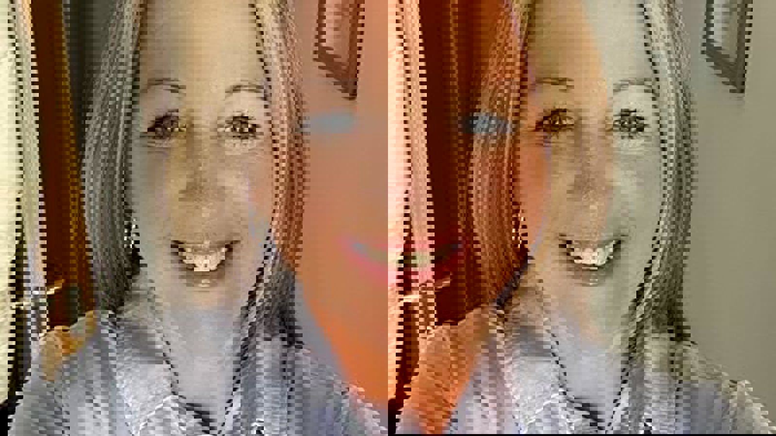 A person with long blonde hair wearing a grey shirt and smiling for a selfie