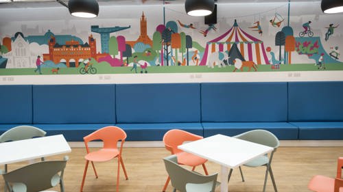 Tables with bright orange and green chairs with a colourful circus themed murals on the back wall