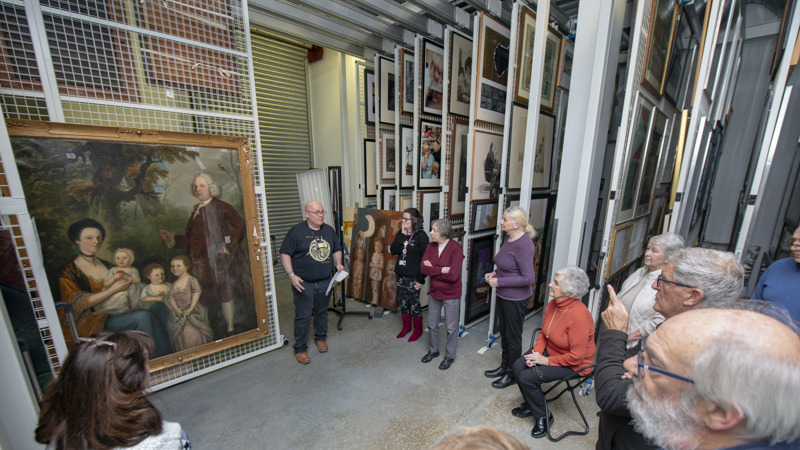 Photograph shows a group tour in progress at Glasgow Museums Resource Centre in the painting store