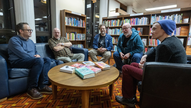 Five people sitting on chairs and a sofa in a circle during a book group in library.