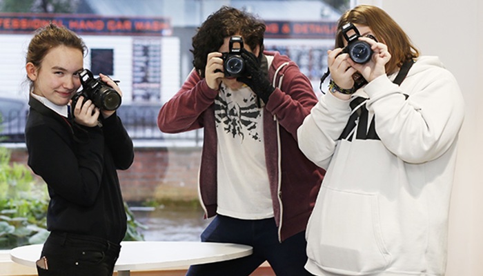 Three people hold cameras to their faces and pretend to take a picture of the person who is photographing them. 