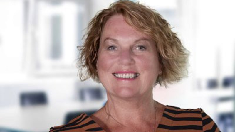 A headshot of Jan Buchanan, a person with blonde wavy hair wearing a brown and black striped top