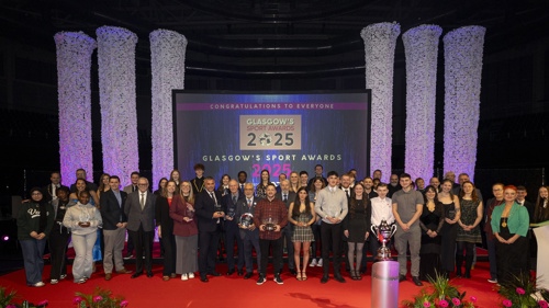People stand on a red carpet in front of a large screen at an awards ceremony